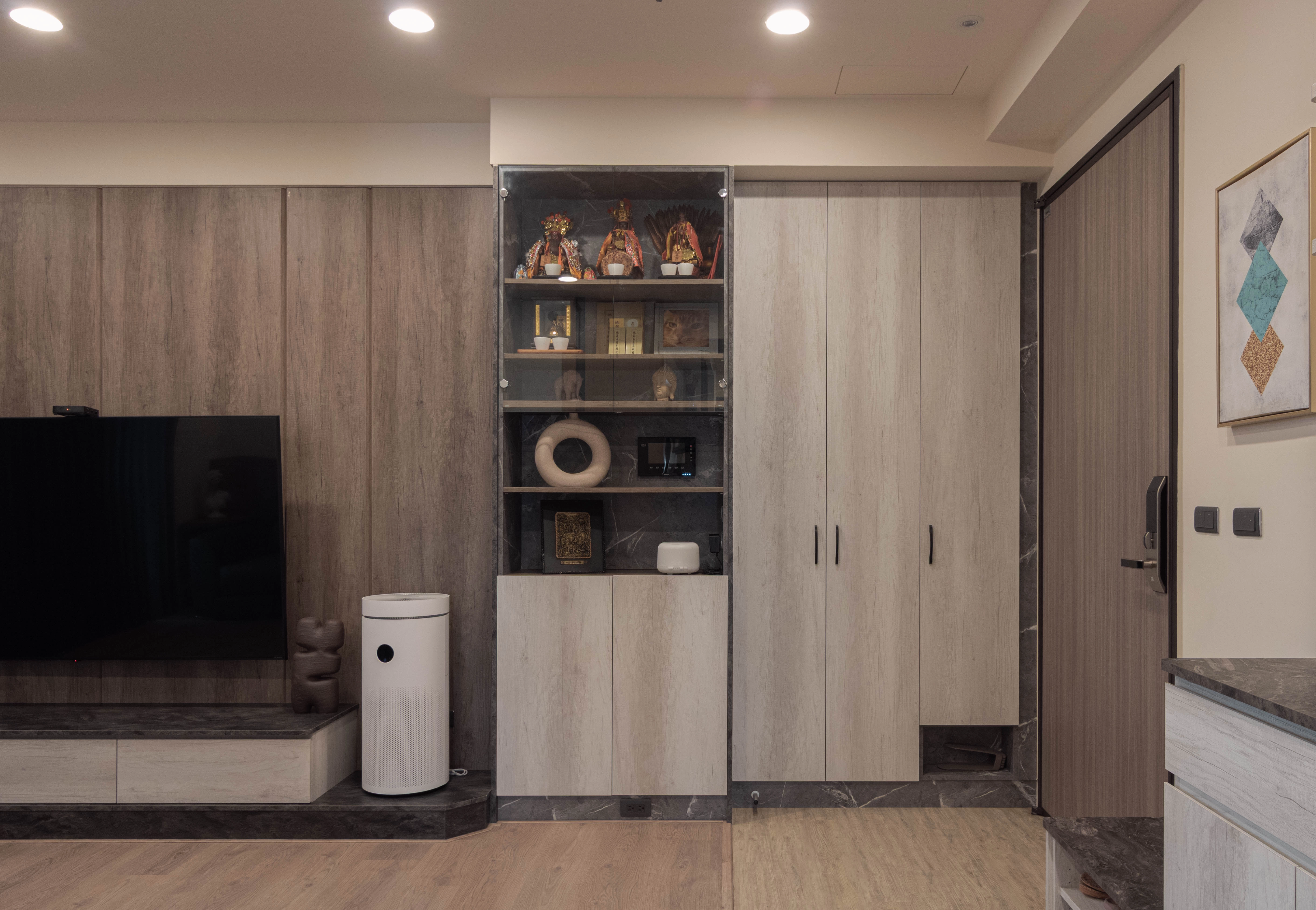 玄關系統開門高櫃搭玻璃門片。客廳沙發木作半高牆區隔，增加視覺層次。